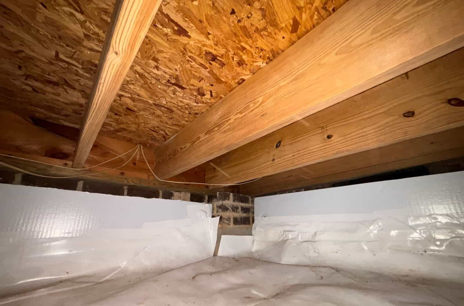 Crawl space corner with white foam board on the walls and white liner covering the floor.