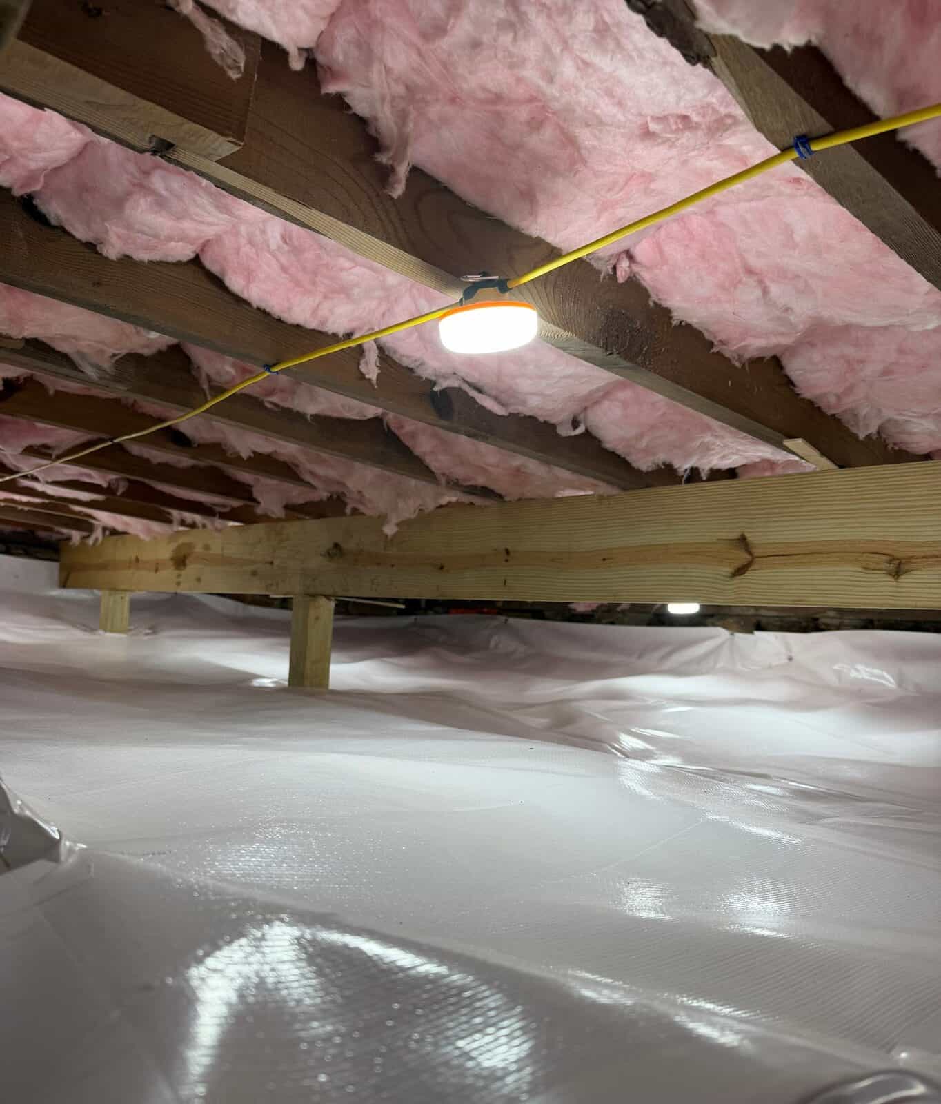 New wood beam on posts above a white lined crawl space floor with a work light on the joists.
