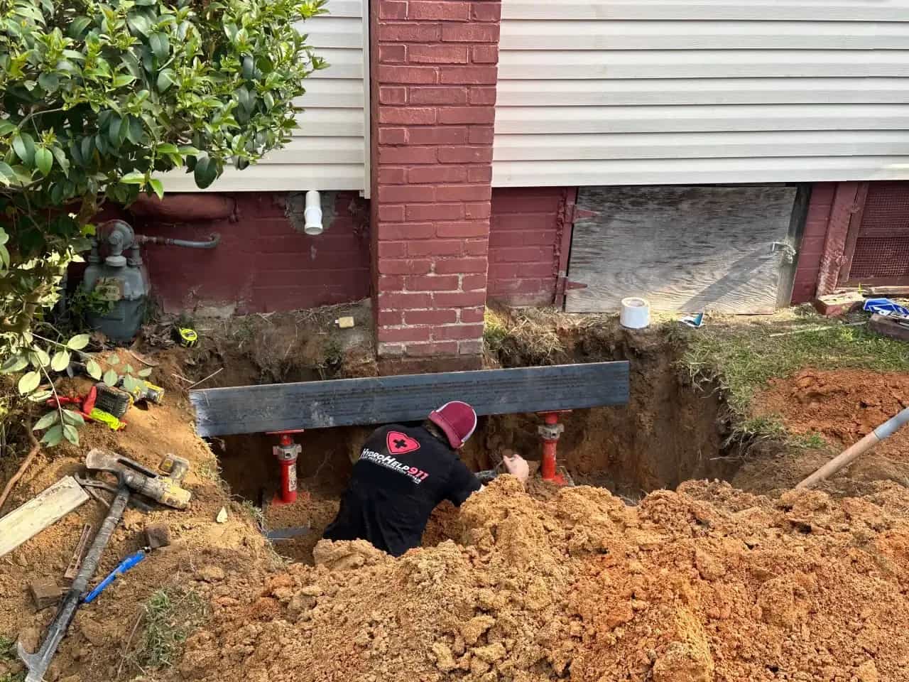 A HydroHelp911 crew member setting red adjustable jacks under a steel beam beside a brick chimney