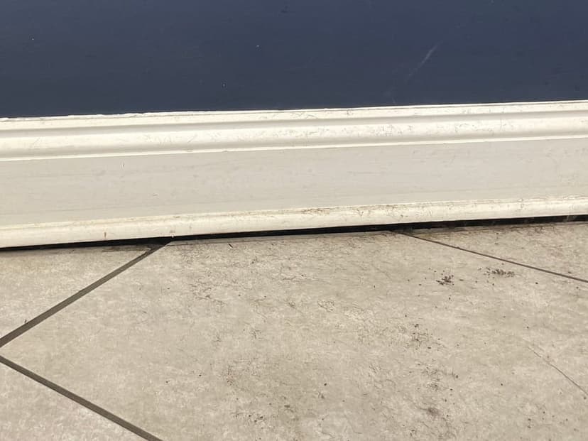 A gap under a baseboard where the tile floor has dropped away from the wall