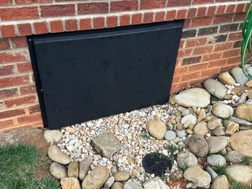 A black crawl space access door set in a brick foundation wall