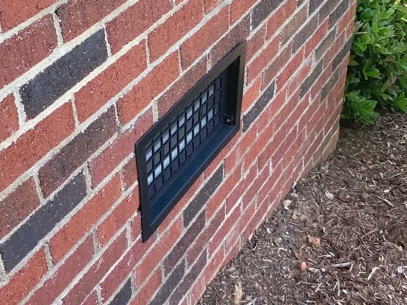 A crawl space vent with a black cover set in a brick foundation wall