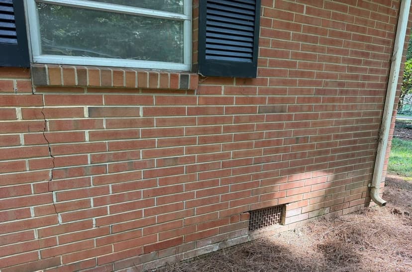 A crack running down a brick wall from the corner of a window