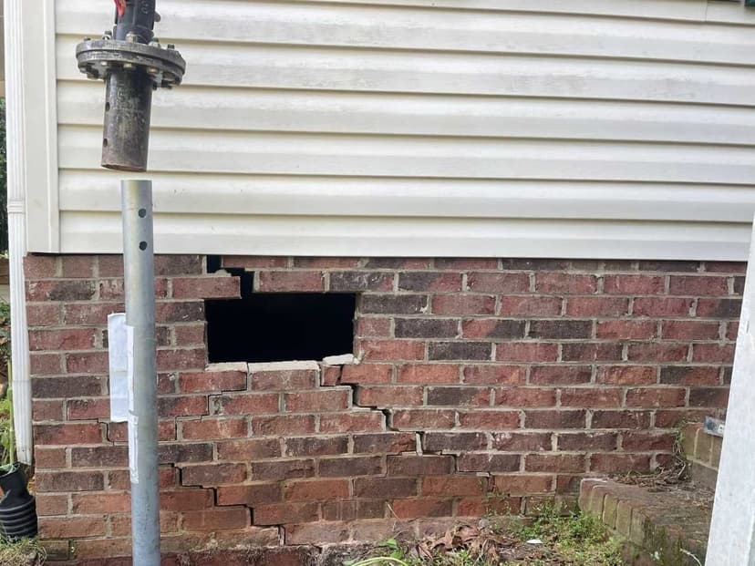 A helical pier shaft with its screw shaped plate in an excavation beside a cracked brick foundation