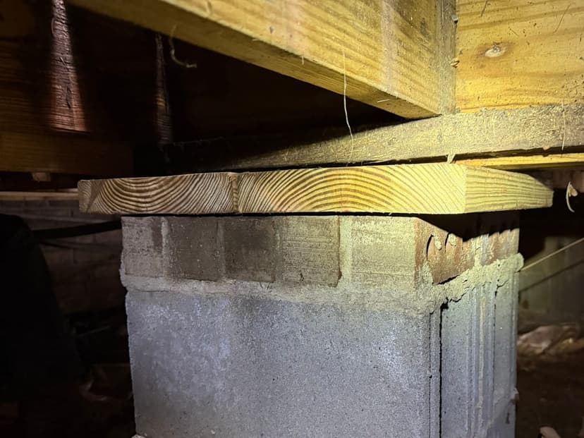 A wood beam resting on a concrete block pier in a crawl space