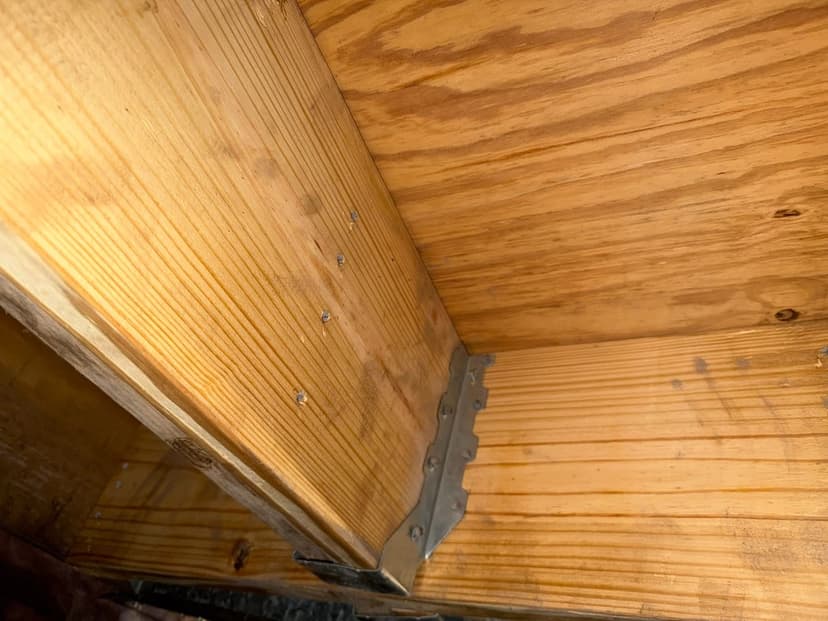 A metal joist hanger at the end of a floor joist under a wood subfloor