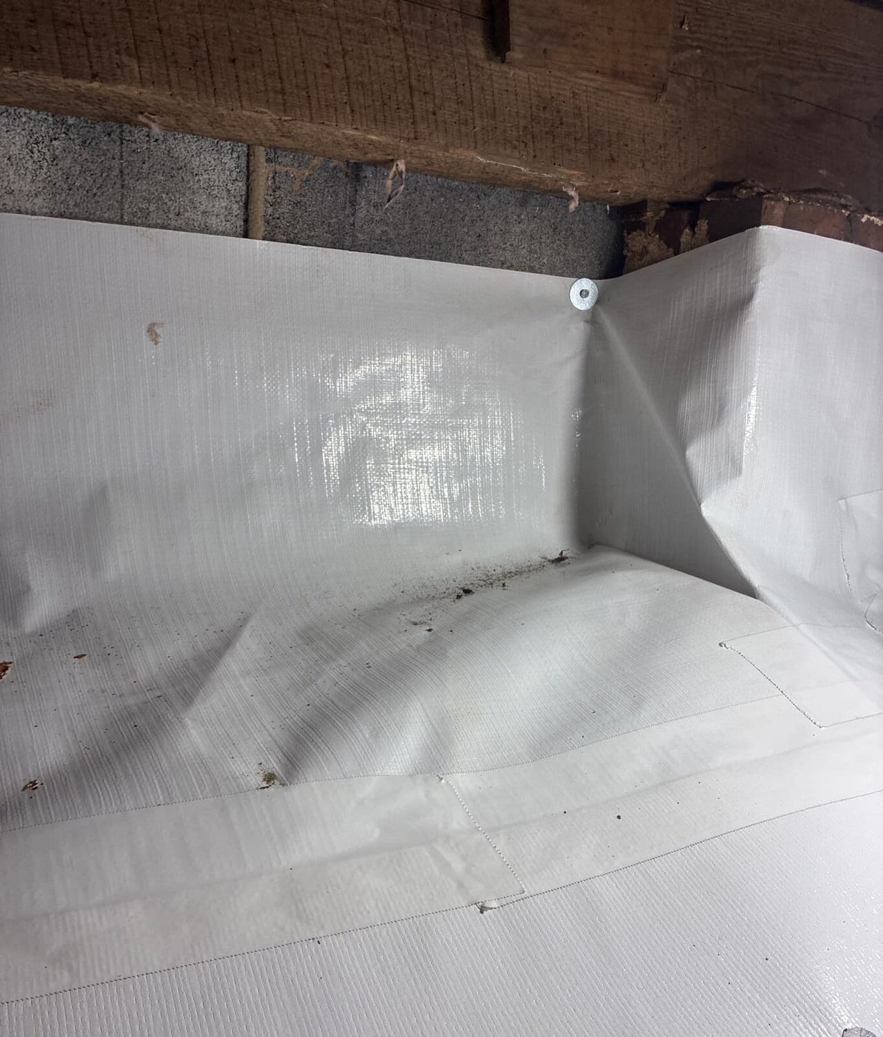 Crawl space corner with white liner fastened to the wall and taped seams across the floor.
