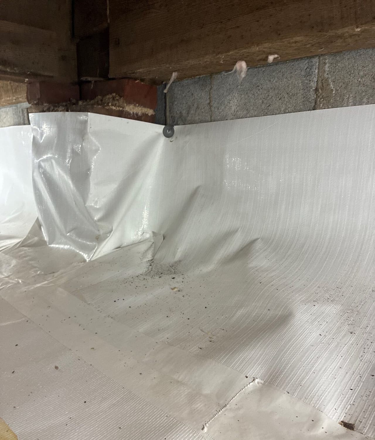 White liner fastened to a block wall below a wood sill, with taped seams on the floor.