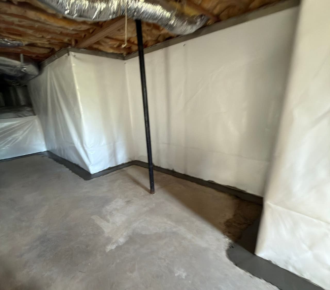 Basement walls covered in white liner with a fresh concrete patch along the floor edge over the drain.