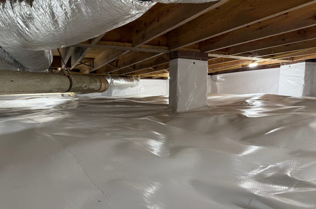 Wide view of a crawl space with white liner over the floor, walls and a support pier.