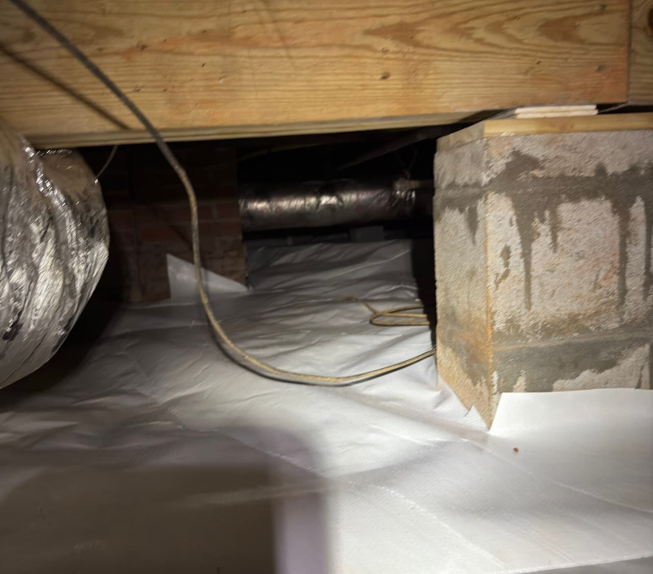 White liner covering a crawl space floor and wrapped around the base of a block pier.