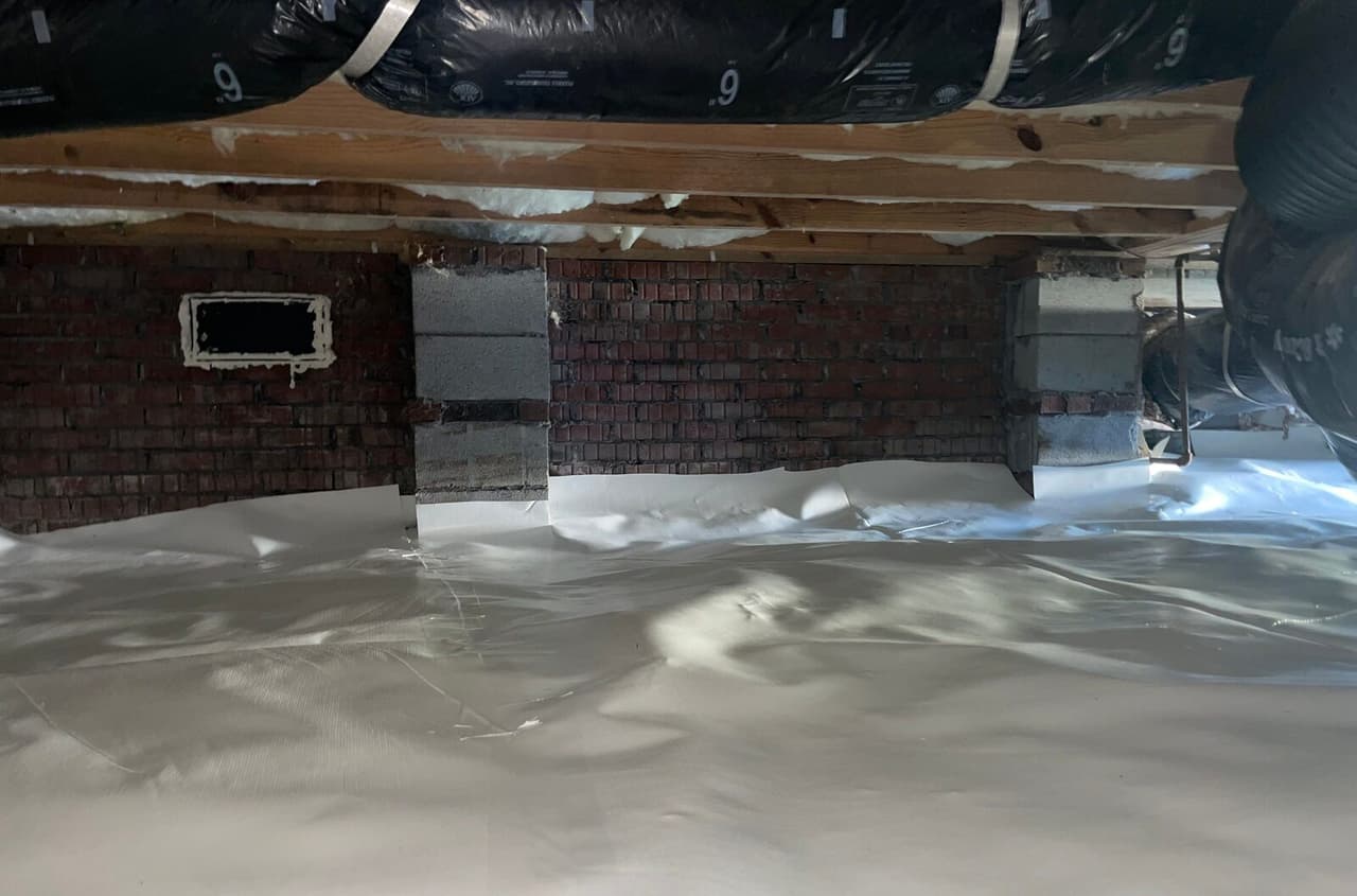 White liner covering the crawl space floor up to brick walls and block piers with a sealed vent.