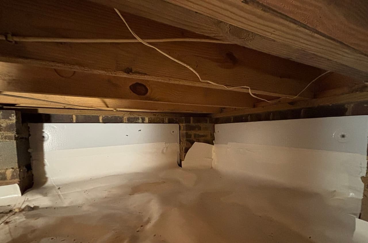 Crawl space with fastened white foam board on the walls and a white liner across the floor.