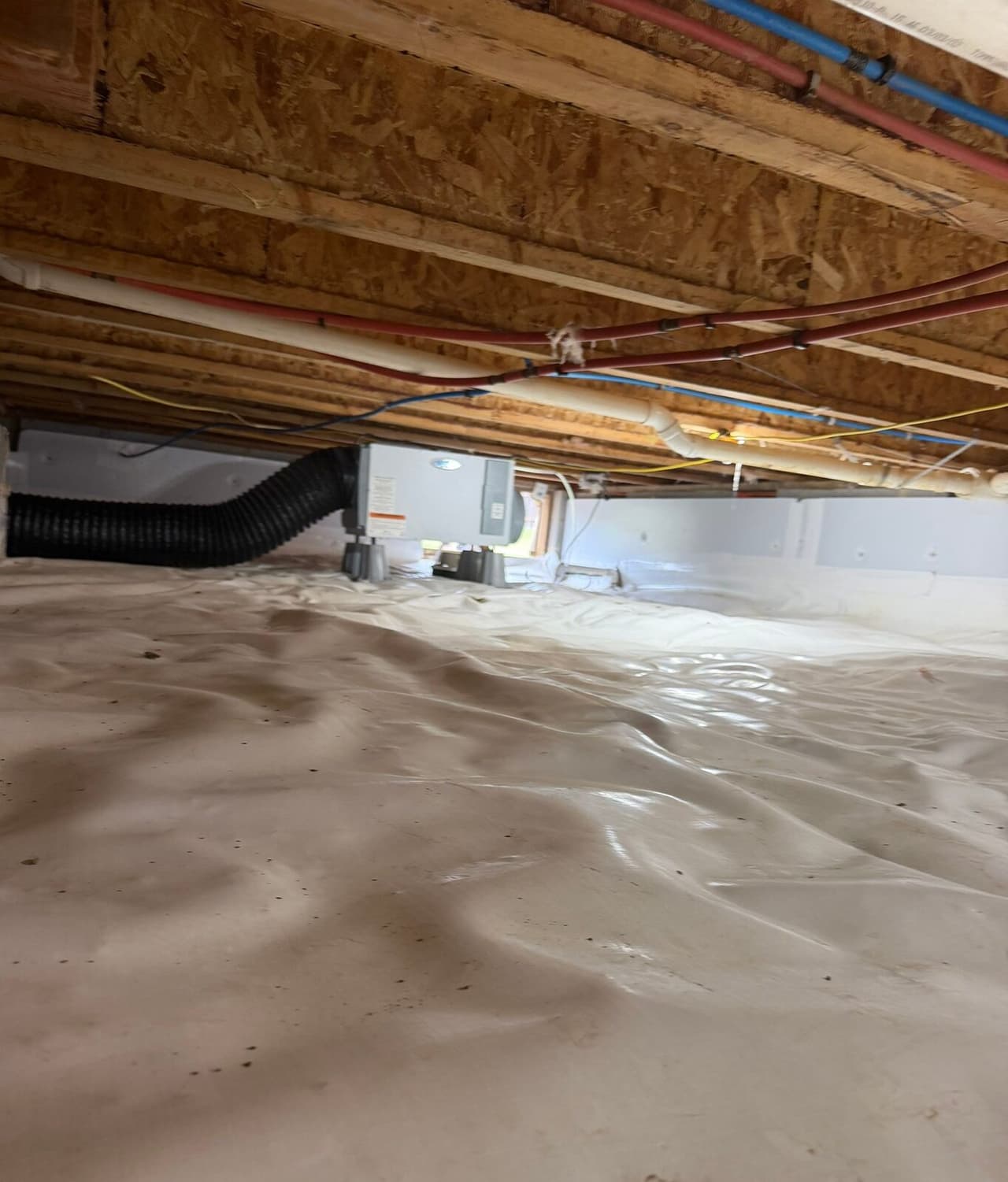 Encapsulated crawl space with white liner, insulated walls and a dehumidifier connected to a black duct.