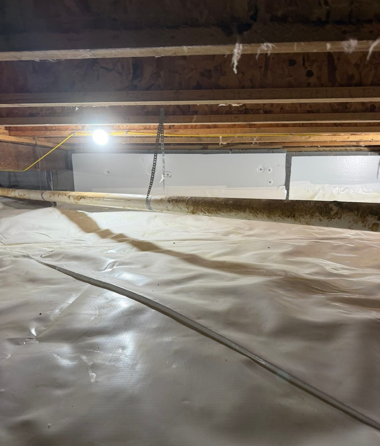 White foam board fastened to crawl space walls above a white floor liner with a pipe in front.