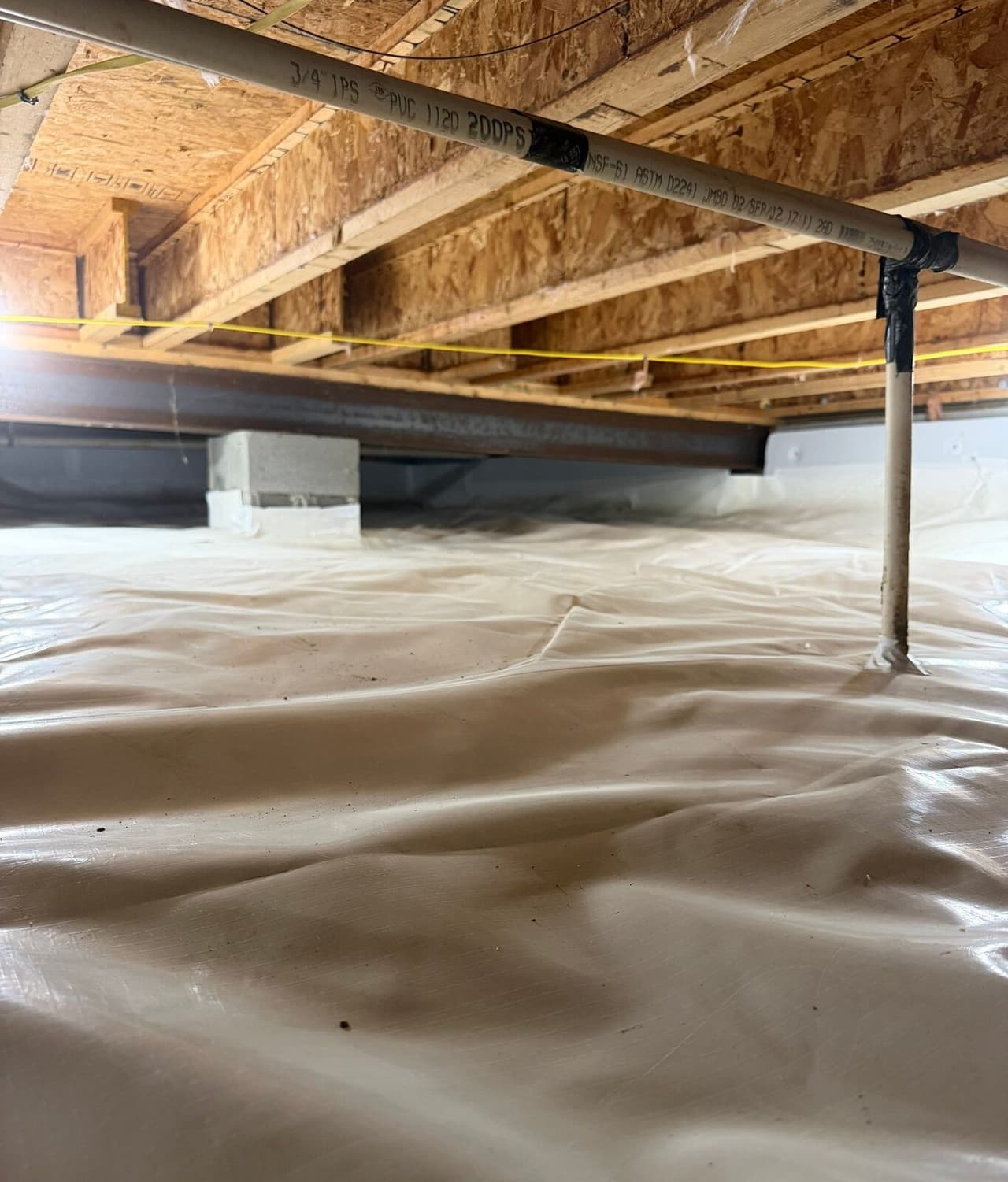 White liner covering a crawl space floor with a pipe support and wrapped pier under a steel beam.