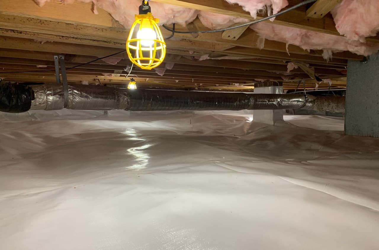 Wide view of a crawl space with a white liner over the floor and up the walls.