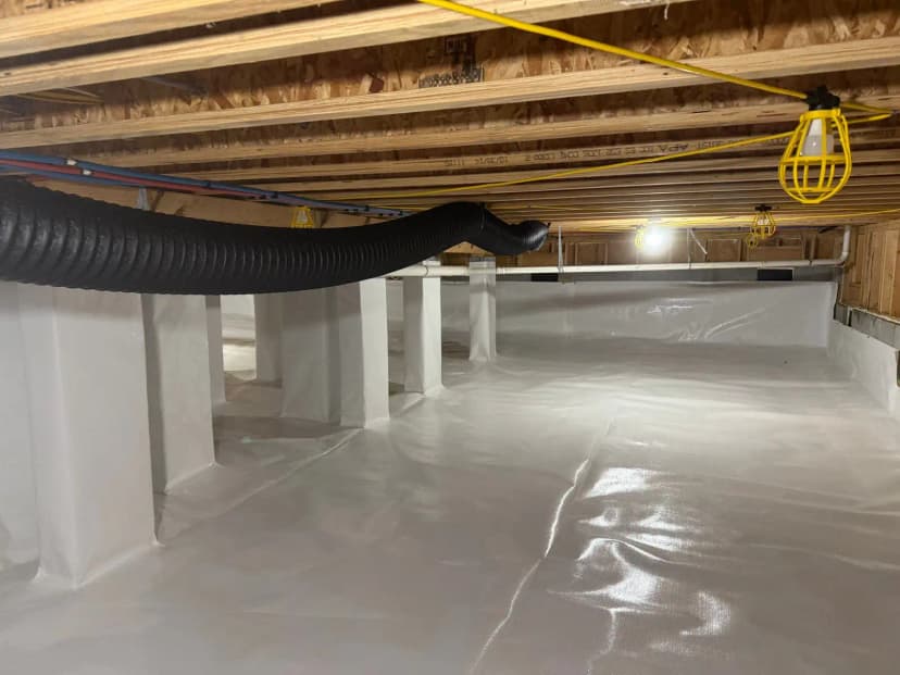 A crawl space with a white vapor barrier over the floor, walls and piers