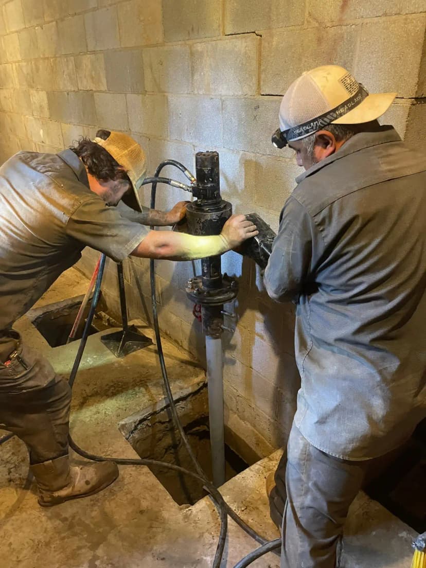 HydroHelp911 Crawl Space & Foundation Repair crew installing helical piers with a rotary drive head in a basement.
