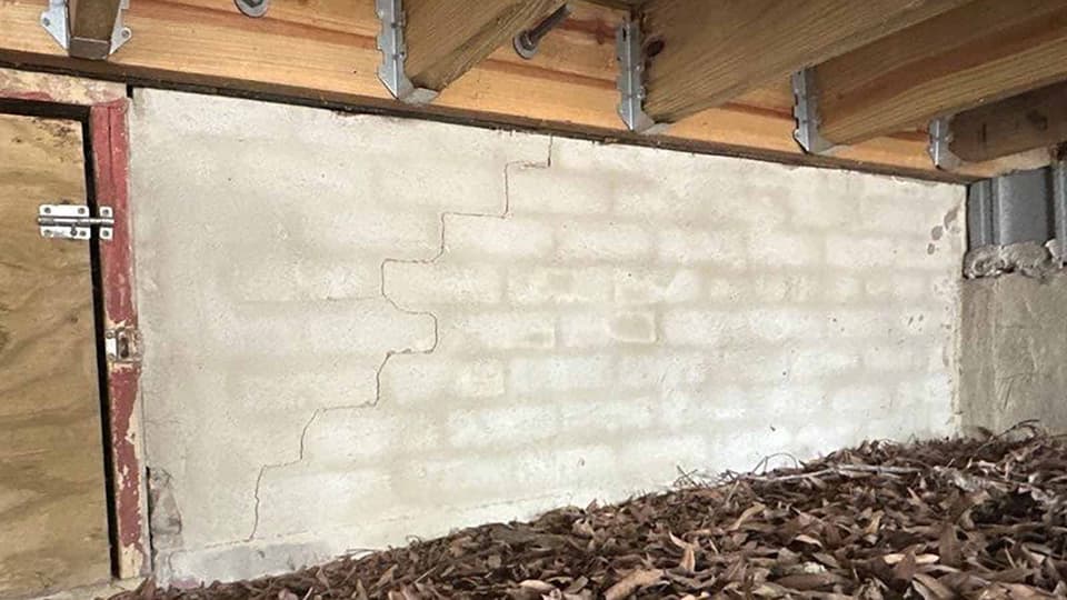 HydroHelp911 Crawl Space & Foundation Repair inspecting a stair step crack in a block foundation wall within a crawl space.