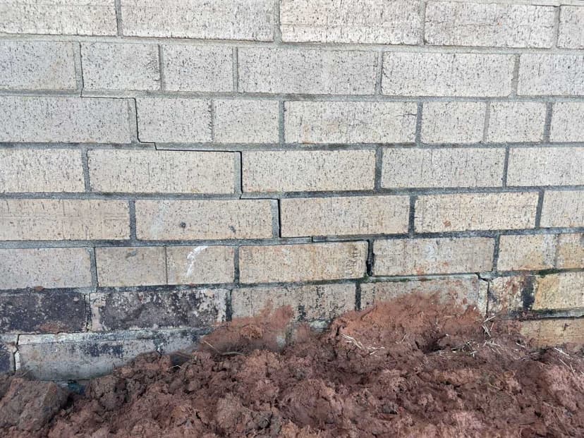 HydroHelp911 Crawl Space & Foundation Repair inspecting a stair step crack in a tan brick foundation wall.