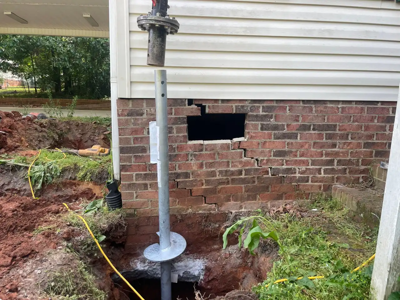 HydroHelp911 Crawl Space & Foundation Repair installing helical piers beside a cracked brick foundation wall.