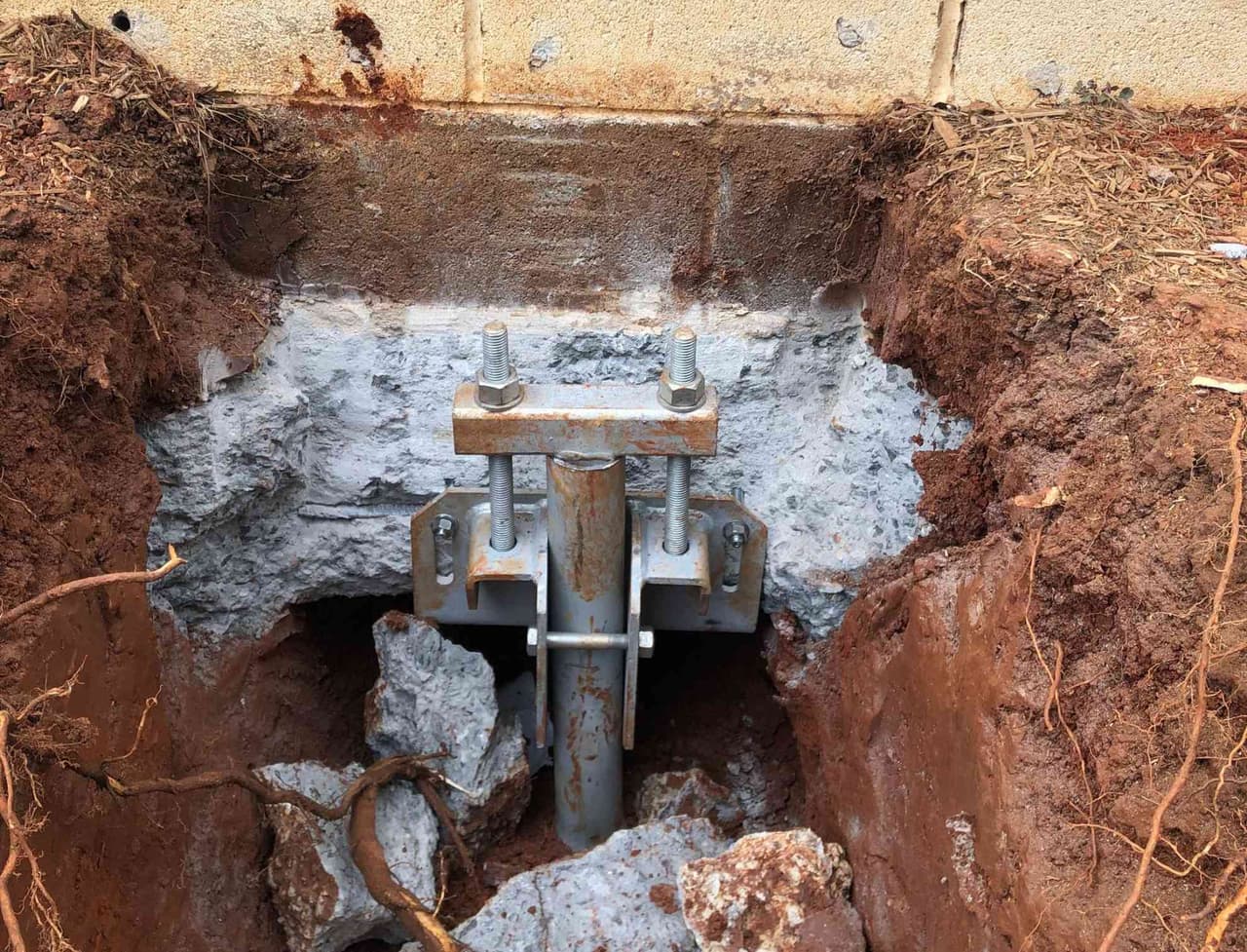 HydroHelp911 Crawl Space & Foundation Repair installing steel piers and footing brackets for foundation underpinning.