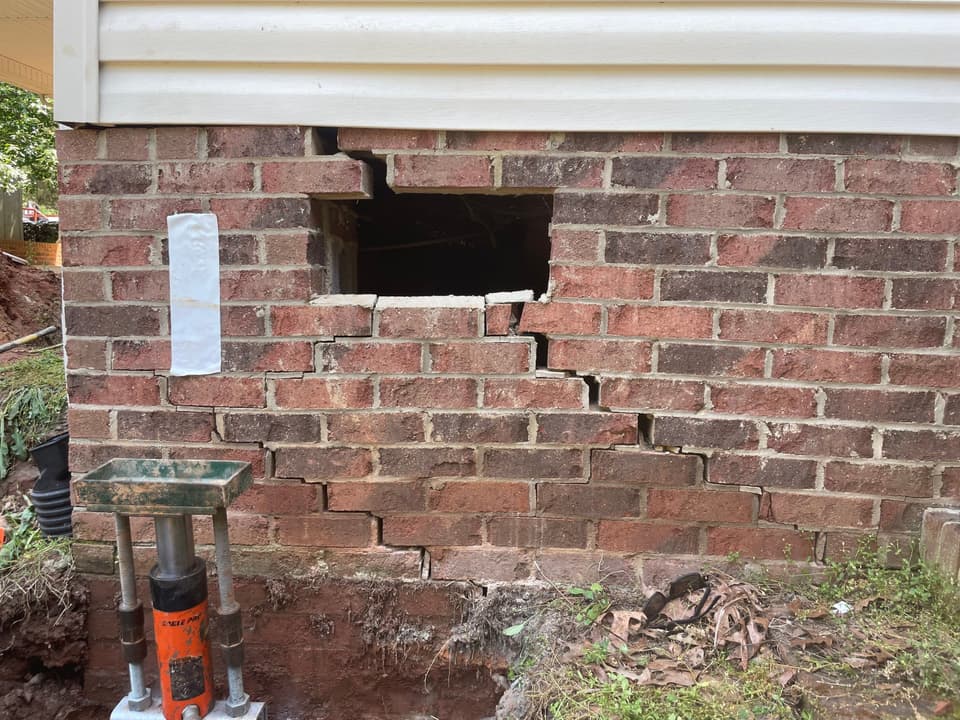 HydroHelp911 Crawl Space & Foundation Repair installing steel piers with a hydraulic ram to repair stair step cracks.