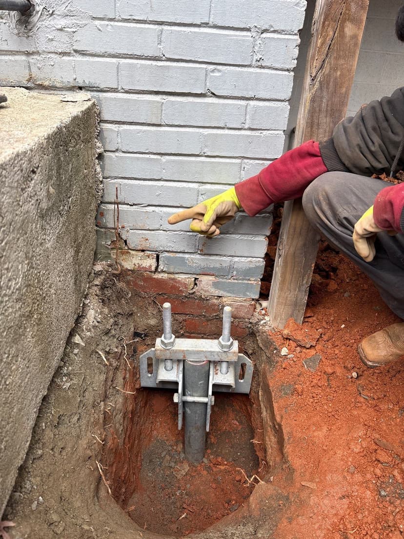 HydroHelp911 Crawl Space & Foundation Repair installing a steel pier with a footing bracket at a brick foundation.
