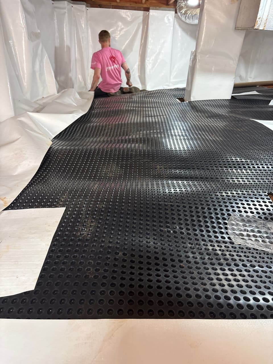 HydroHelp911 Crawl Space & Foundation Repair crew installing a drainage matting over a vapor barrier in a crawl space.