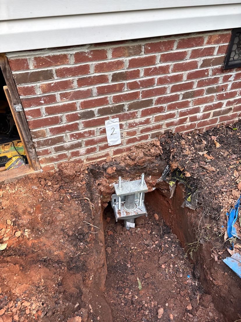 HydroHelp911 Crawl Space & Foundation Repair installing a steel pier for foundation underpinning at a home's exterior.
