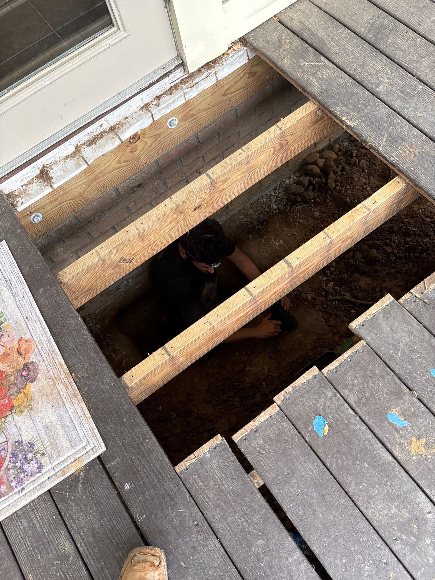 HydroHelp911 Crawl Space & Foundation Repair team member working in an excavation under a deck in Greensboro.