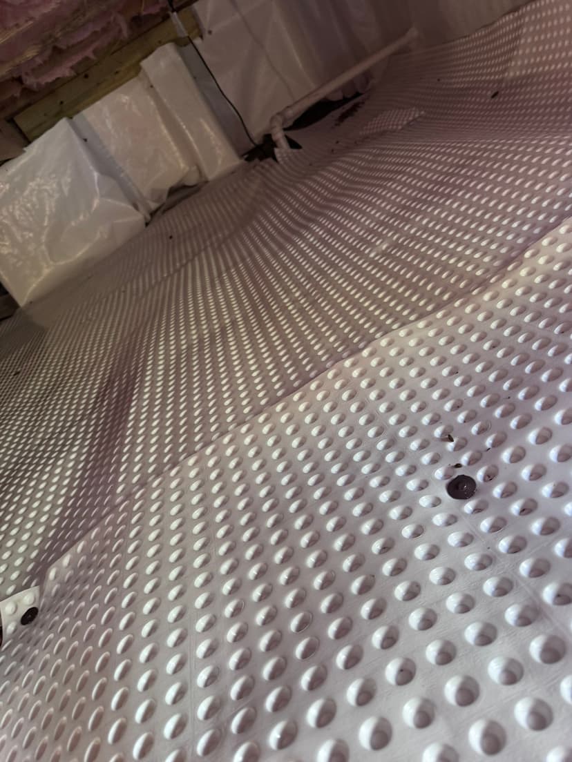HydroHelp911 Crawl Space & Foundation Repair installing drainage matting and a vapor barrier in a crawl space.
