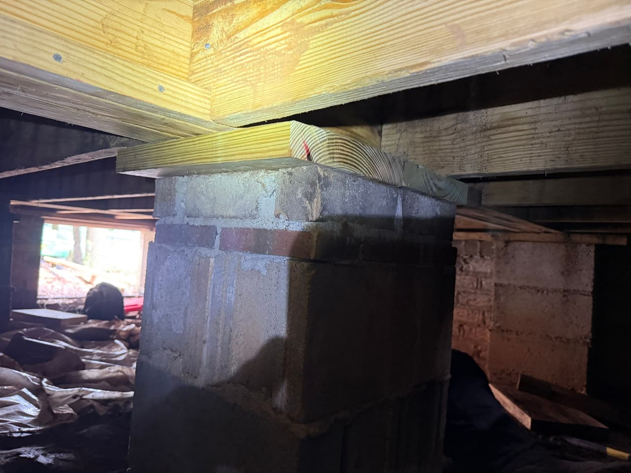 HydroHelp911 Crawl Space & Foundation Repair stabilizing floor joists with wooden shims on a brick pier.