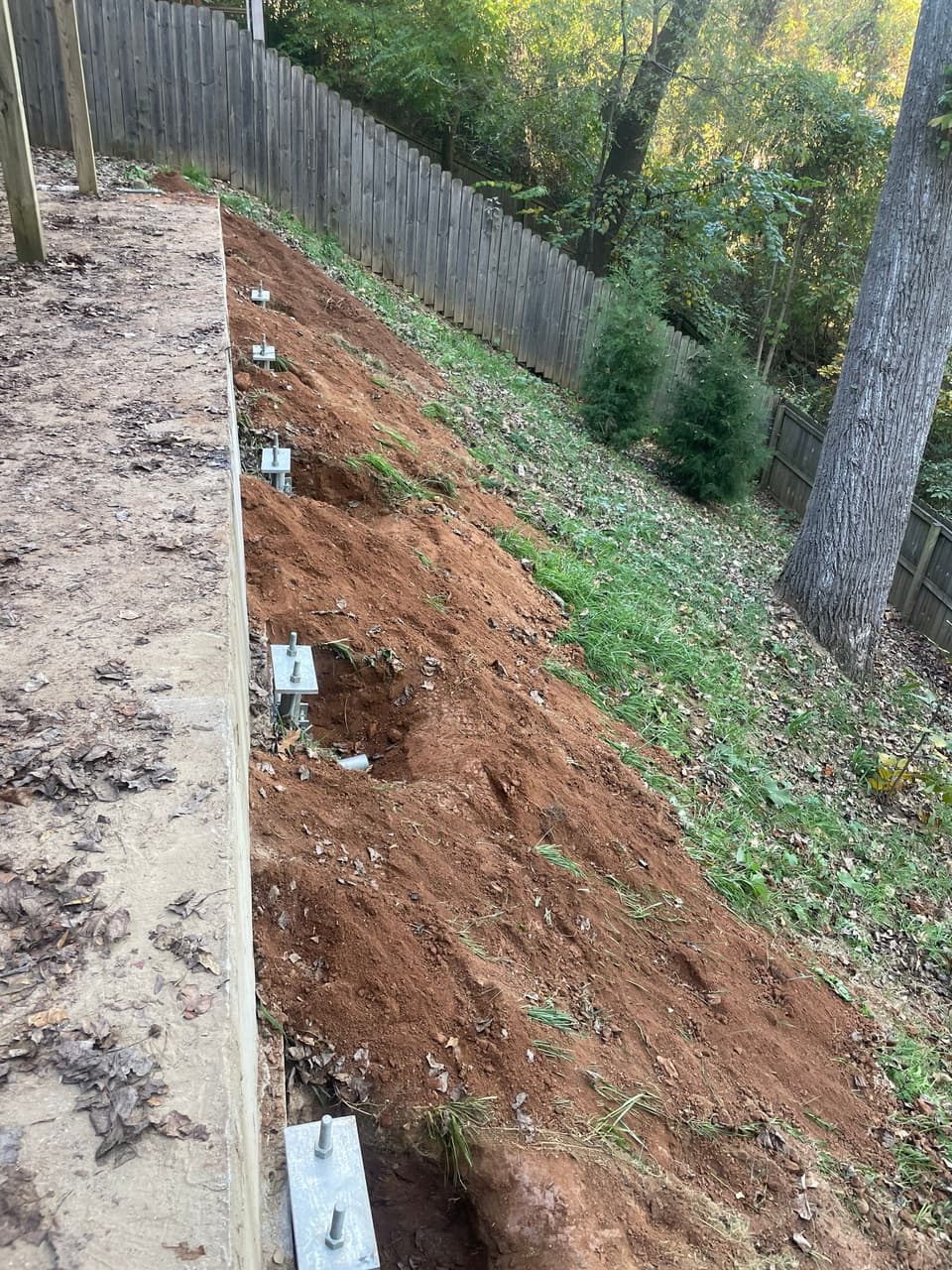 HydroHelp911 Crawl Space & Foundation Repair crew installing slab piers along a foundation, next to a wooded hillside.