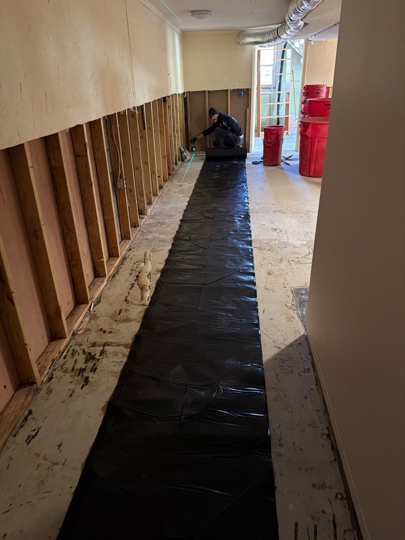 HydroHelp911 Crawl Space & Foundation Repair crew installing interior basement waterproofing along a framed wall.