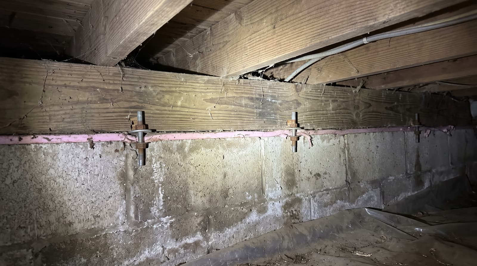 HydroHelp911 Crawl Space & Foundation Repair inspecting efflorescence on a foundation wall in a crawl space with wood joists.