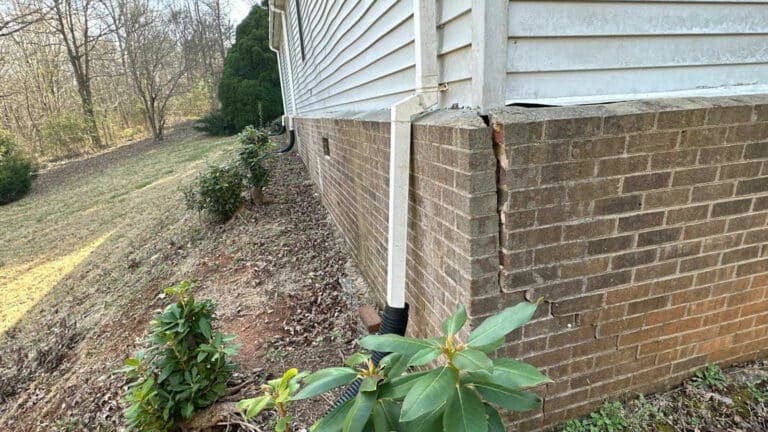 A wide vertical crack separates a brick corner wall on a house exterior with white siding.