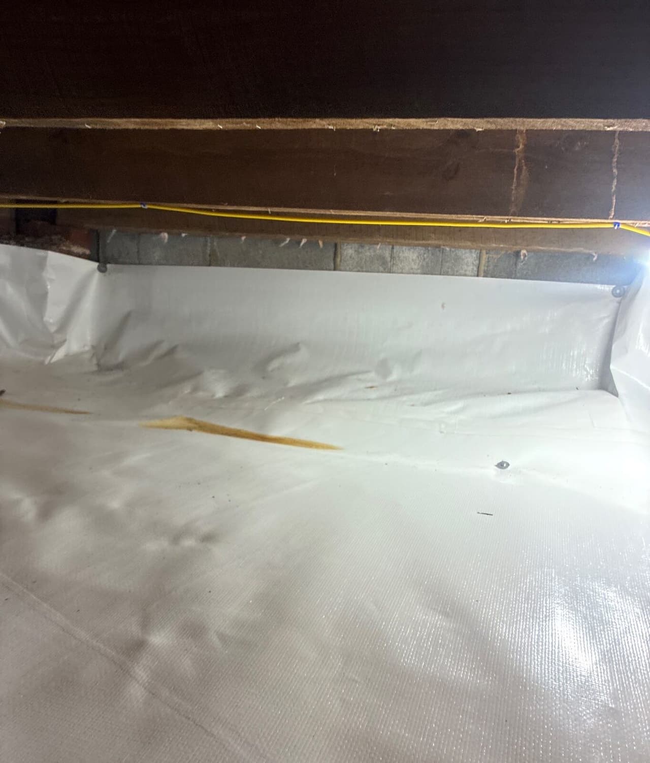 White liner fastened along a block wall and covering the crawl space floor below wood framing.