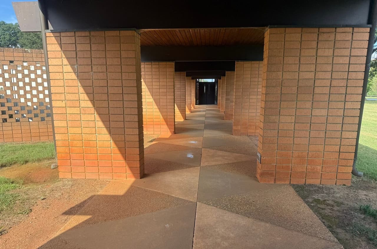 Long brick colonnade walkway with concrete slabs showing patched injection holes.