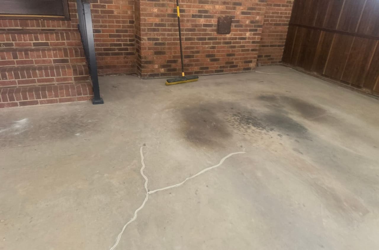 Garage floor with a branching crack filled with white sealant beside brick steps and a broom.