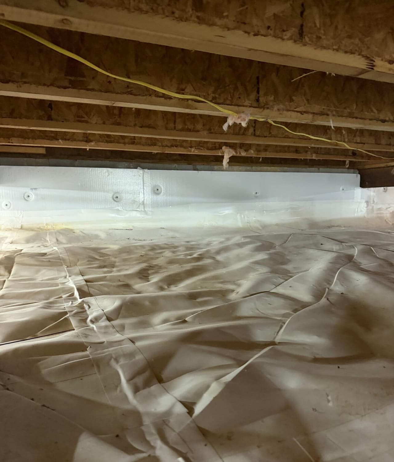 White foam board panels on a crawl space wall meeting a white liner covering the floor.